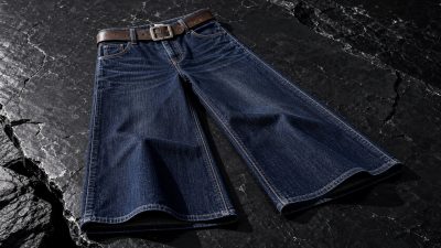Neatly folded stack of dark indigo wide-leg jeans beside wooden hanger and tailor's measuring tape on a clean minimalist surf