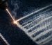 Industrial laser etching a fade pattern onto indigo denim, soft natural light, minimalist composition