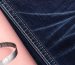 Macro shot of indigo denim fabric with laser-etched fade lines and visible stitching, soft natural light