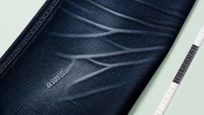 Stack of indigo jeans on wooden hanger beside tailor tape in soft natural light