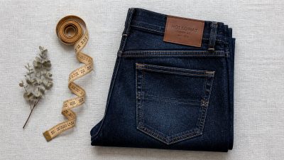 A neatly folded stack of indigo jeans with a tailor's measuring tape resting on top in soft natural light