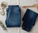 Neatly folded stack of indigo jeans on rustic wooden table beside a tailor tape measure in soft natural light