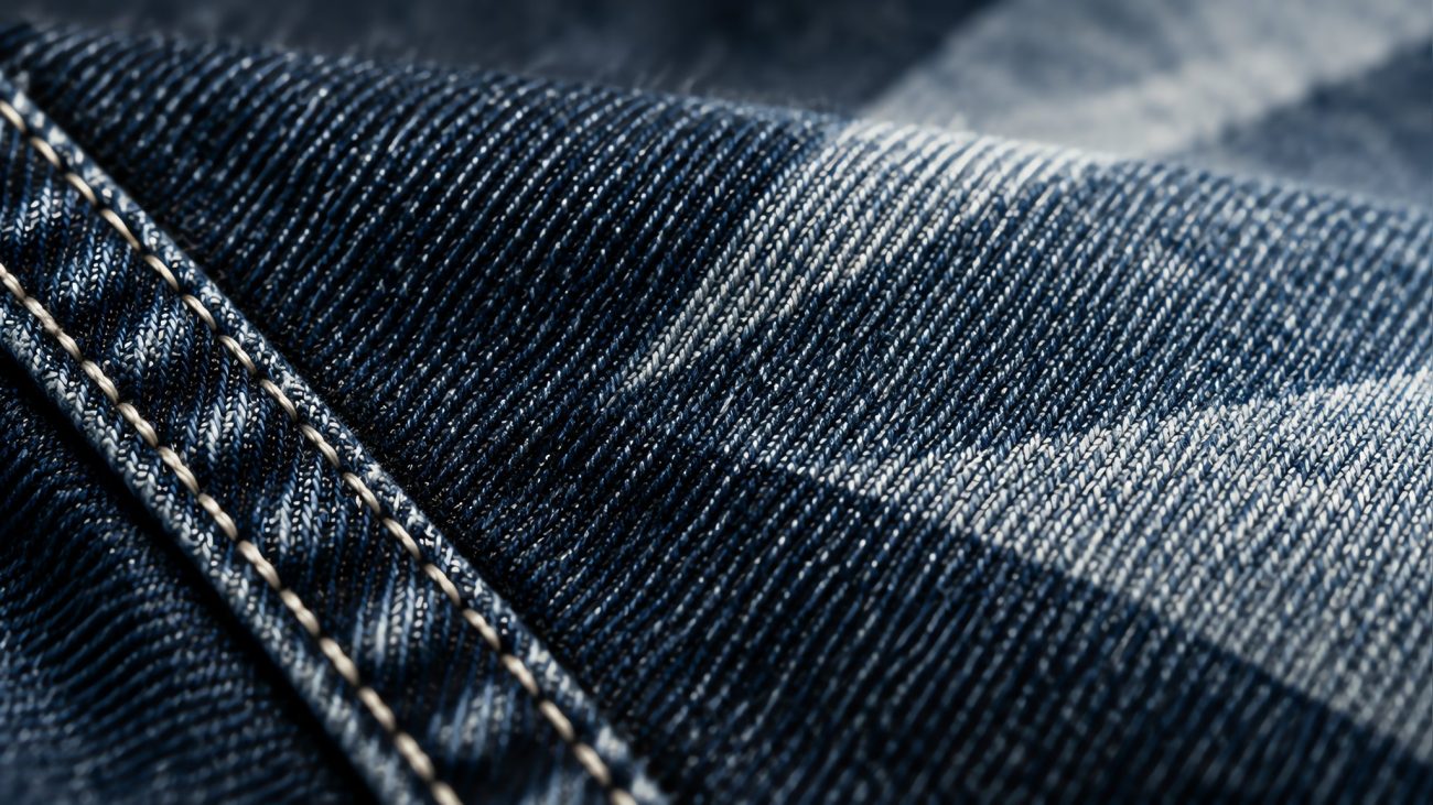 Stack of indigo jeans on a wooden table beside a tailor's measuring tape in soft natural light