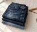 Neatly folded stack of indigo jeans beside a wooden hanger and tailor tape on neutral linen in soft natural light