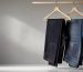 Stack of folded indigo jeans on a wooden hanger beside a tailor measuring tape in soft natural light