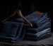 Pair of indigo jeans hanging on a wooden hanger against a plain white wall, soft daylight, minimalist