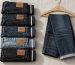 Neatly folded stack of indigo jeans on a wooden shelf beside a tailor tape in soft natural light