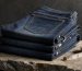 Stack of folded indigo jeans beside a wooden hanger and tailor tape on a light oak table in soft daylight